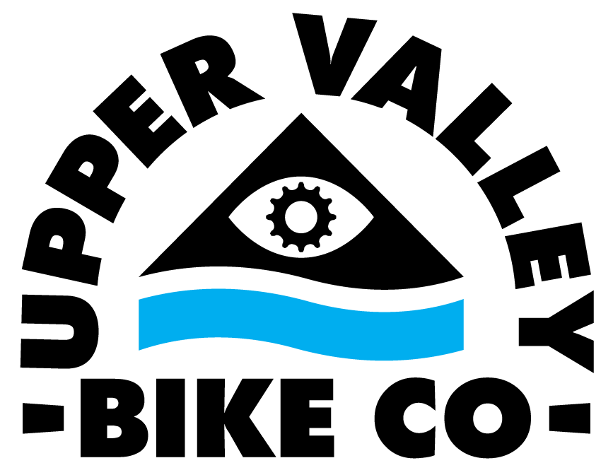 Logo graphic with the words Upper Valley Bike Co surrounding a black triangle above a blue wave. There is an eye shape in the center of the triangle, with a gear shape as the eye's iris.