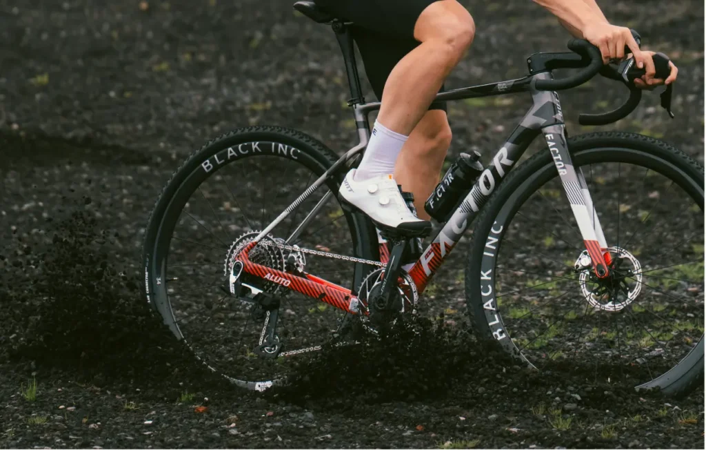 Action photo of a person riding a bicycle in loose gravel. Only the person's legs and arms are visible.
