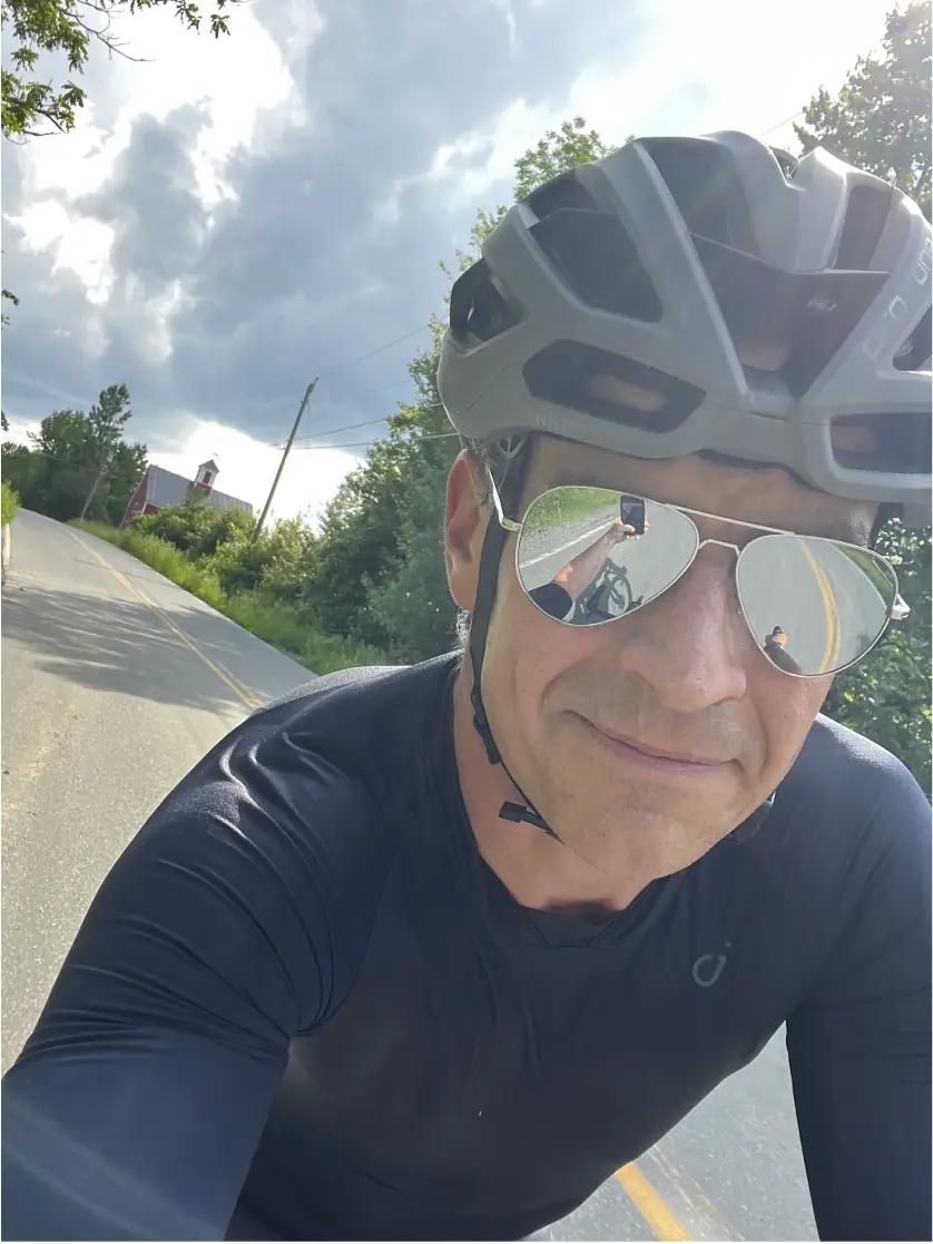 Selfie photo of James Allen wearing a bike helmet and sunglasses, while riding on a paved road. Bicycle fitting and bike builds in Vermont.