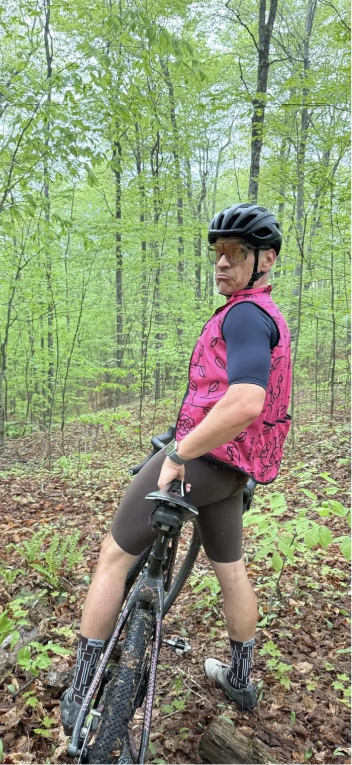 James Allen wearing a bike helmet and sunglasses, sitting on a stopped bicycle in a forest.