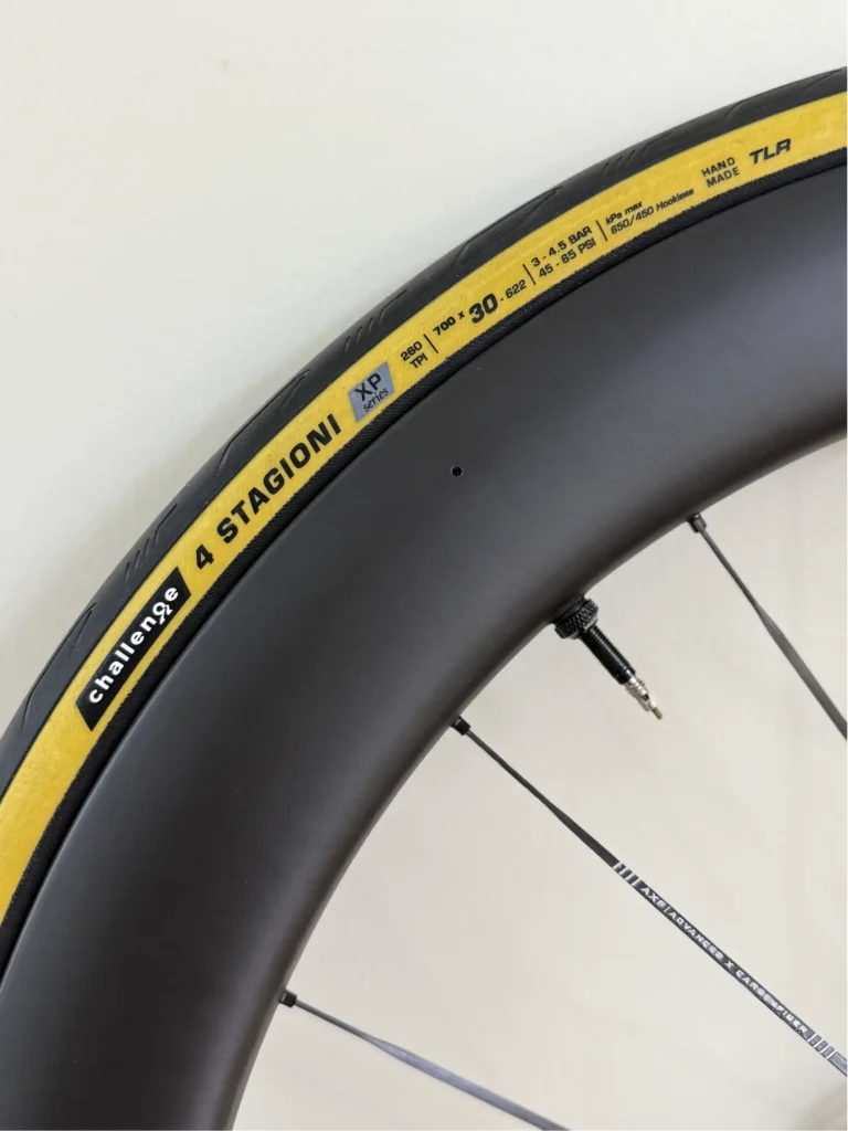 Closeup side view of an all-season road tire. The text on the wheel says Challenge 4 Stagioni XP Series.